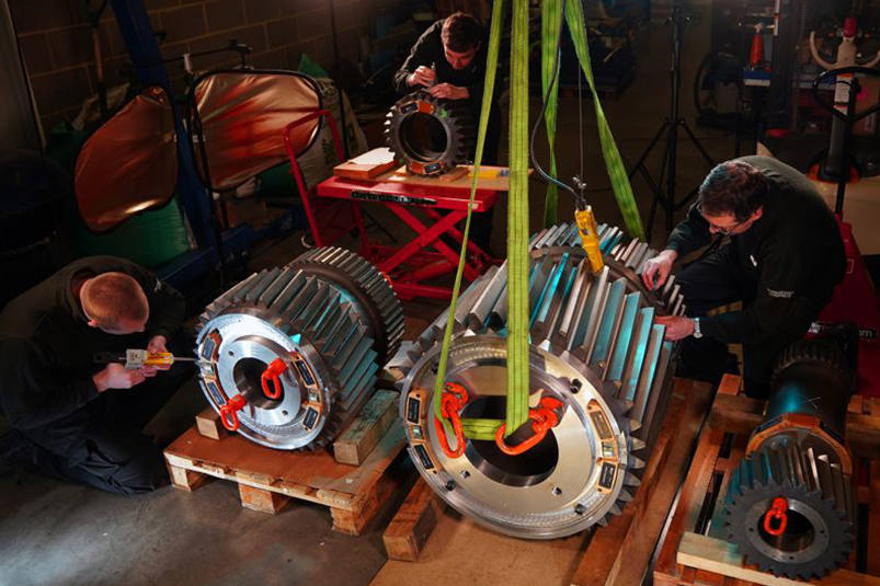 Three engineers working on several gear boxes installing the gear alignment system using various tools.