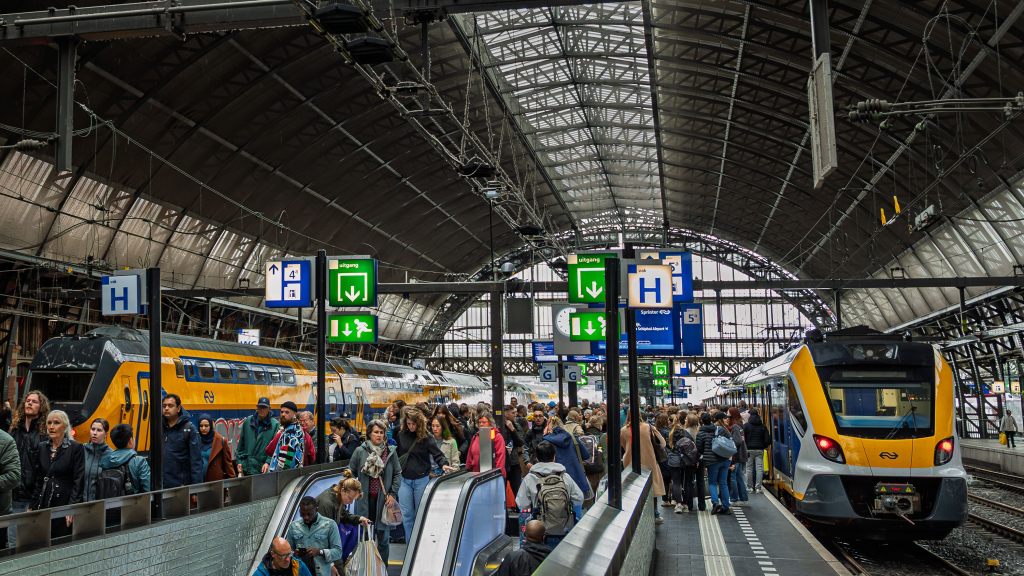Passengers using escalators inside a busy railway station.